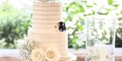 A two-tier white wedding cake with floral decorations and a Mr & Mrs sign on a table.