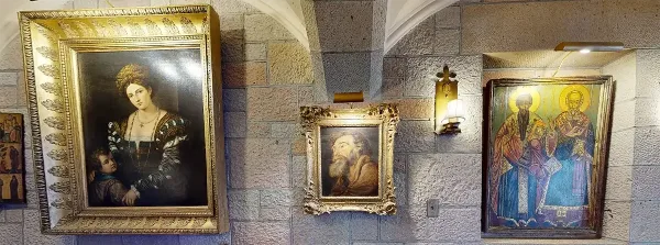Interior view of a stone-walled castle room displaying framed classical paintings and religious art.