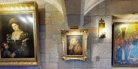Interior view of a stone-walled castle room displaying framed classical paintings and religious art.