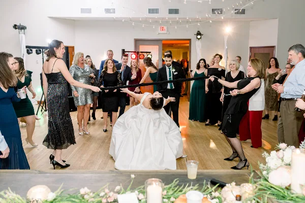 A bride and groom participating in a ribbon-cutting game on a dance floor at a wedding reception.