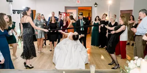 A bride and groom participating in a ribbon-cutting game on a dance floor at a wedding reception.