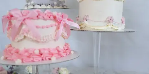 A display of three decorated cakes on stands surrounded by cupcakes and small pastries on a table.