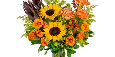 A floral arrangement featuring yellow sunflowers, orange roses, and greenery in a clear glass vase.