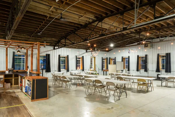 Interior view of a spacious event hall with high wooden ceilings, string lights, and tables set up for a gathering.