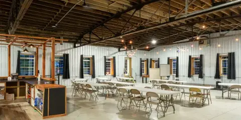Interior view of a spacious event hall with high wooden ceilings, string lights, and tables set up for a gathering.