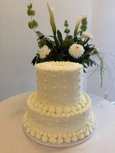A two-tier white wedding cake decorated with piped frosting and fresh flowers.
