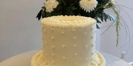 A two-tier white wedding cake decorated with piped frosting and fresh flowers.
