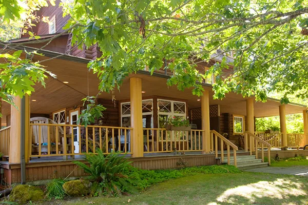 Exterior view of a rustic wooden lodge with a covered porch and surrounding greenery.