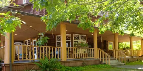 Exterior view of a rustic wooden lodge with a covered porch and surrounding greenery.