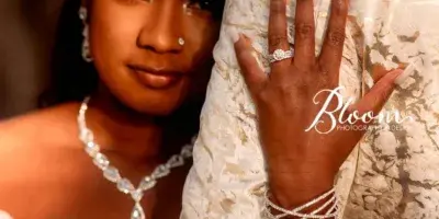 A bride and groom in wedding attire, with the bride wearing a white dress and jewelry, leaning against the groom in a patterned suit.