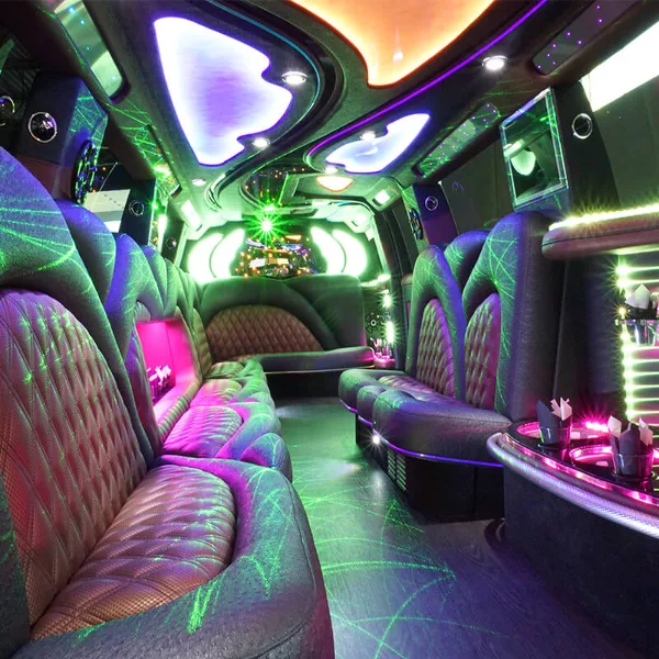 Interior view of a party bus featuring purple and green ambient lighting, plush leather seating, and a bar area.