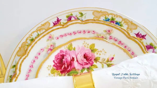 A stack of vintage floral china plates with gold rims and a white napkin.