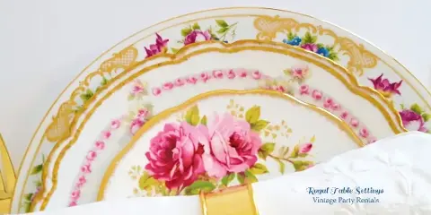 A stack of vintage floral china plates with gold rims and a white napkin.