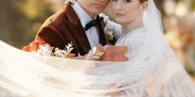 A bride and groom posing together in an outdoor setting with autumn foliage in the background.