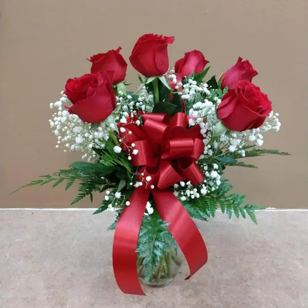 A floral arrangement featuring red roses and baby's breath in a clear glass vase with a red ribbon bow.