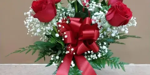 A floral arrangement featuring red roses and baby's breath in a clear glass vase with a red ribbon bow.