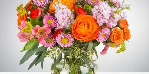 A vibrant mixed bouquet of orange, pink, and red flowers arranged in a clear glass vase.