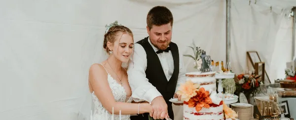 A bride and groom cutting a multi-tiered wedding cake decorated with orange flowers at a wedding reception.