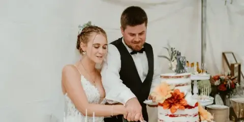 A bride and groom cutting a multi-tiered wedding cake decorated with orange flowers at a wedding reception.
