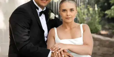 A bride and groom in formal wedding attire sitting on stone steps with a white bouquet.
