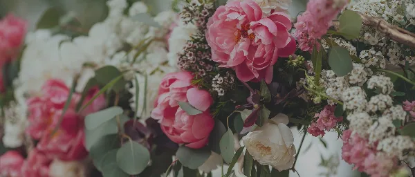 A close-up of a lush floral arrangement with pink peonies, white roses, and greenery.