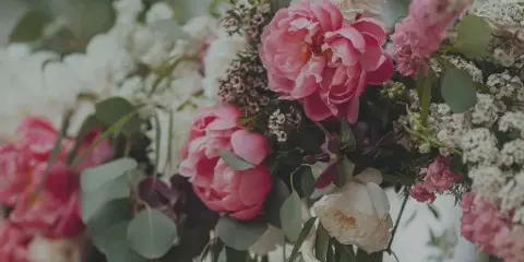 A close-up of a lush floral arrangement with pink peonies, white roses, and greenery.