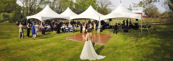 Outdoor wedding reception with white event tents, tables, chairs, and a dance floor on a grassy lawn.