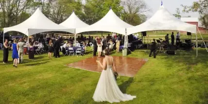 Outdoor wedding reception with white event tents, tables, chairs, and a dance floor on a grassy lawn.