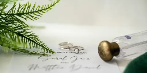 A close-up of a signed wedding certificate with two rings and a quill pen resting on the paper.