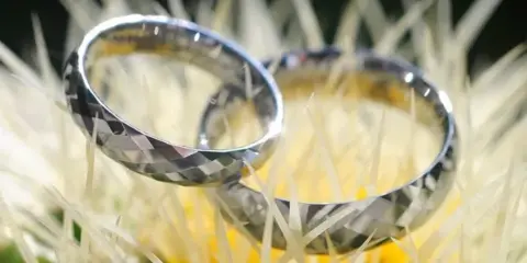 A close-up photograph of two silver wedding rings resting on a yellow flower.