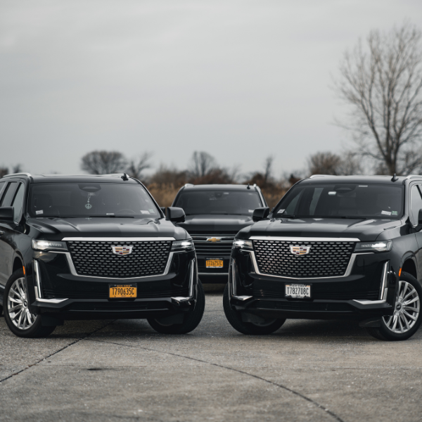 A lineup of black luxury SUVs, including Cadillacs, parked on a paved lot.