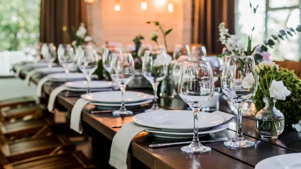 A long wooden table set for a wedding reception with white plates, wine glasses, and floral arrangements.