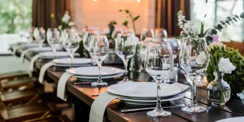 A long wooden table set for a wedding reception with white plates, wine glasses, and floral arrangements.