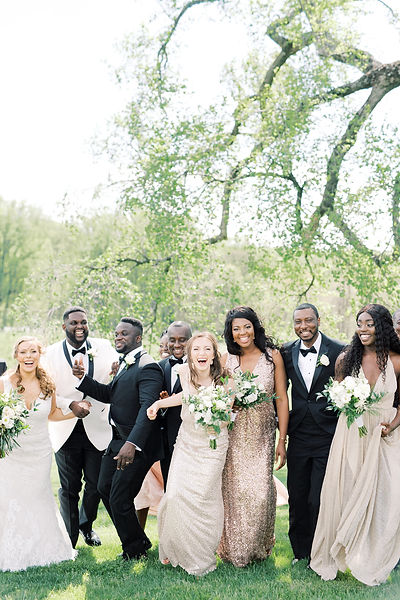 A wedding party including the bride and groom posing outdoors on a grassy lawn with large trees in the background.