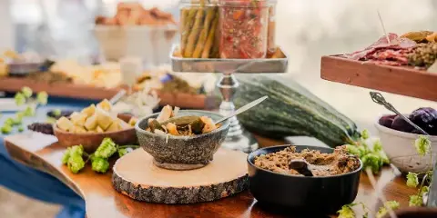 A rustic catering table featuring bowls of seasonal vegetables, dips, and charcuterie arranged on wooden boards and platters.