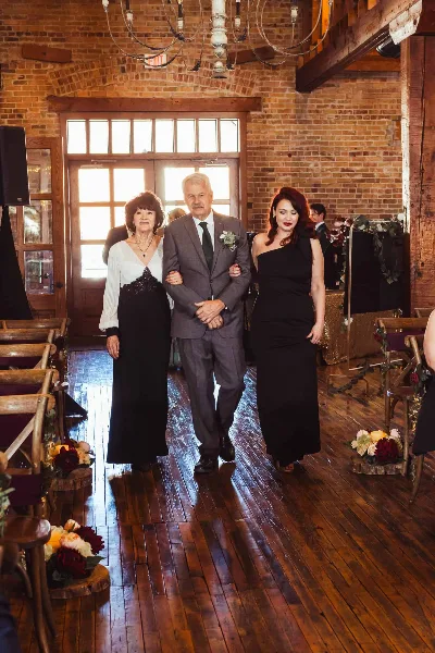 A wedding party walking down the aisle in a rustic event venue with exposed brick walls and wooden floors.