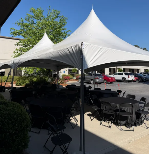 White event tent set up outdoors with black tables and chairs arranged underneath.