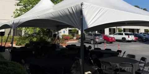 White event tent set up outdoors with black tables and chairs arranged underneath.