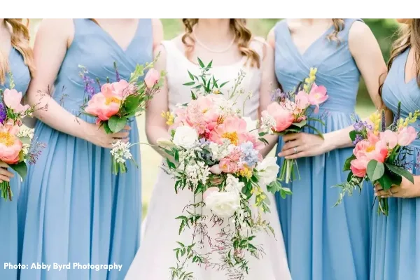 A bride and bridesmaids in blue dresses holding pink and white floral bouquets.