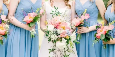 A bride and bridesmaids in blue dresses holding pink and white floral bouquets.