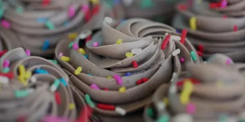 A close-up photograph of chocolate-frosted cupcakes topped with colorful sprinkles.