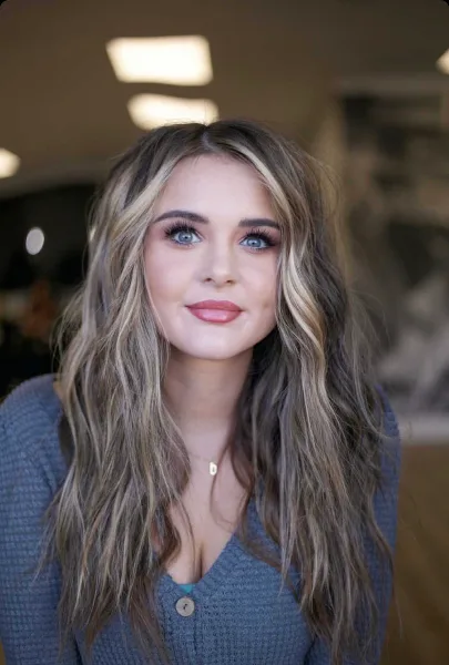 Portrait of a woman with long, wavy highlighted hair and professional makeup.