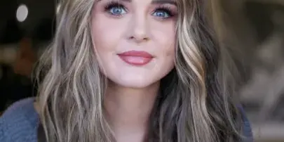 Portrait of a woman with long, wavy highlighted hair and professional makeup.