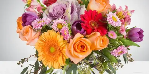 A colorful mixed bouquet of roses, gerbera daisies, tulips, and chrysanthemums arranged in a clear glass vase.