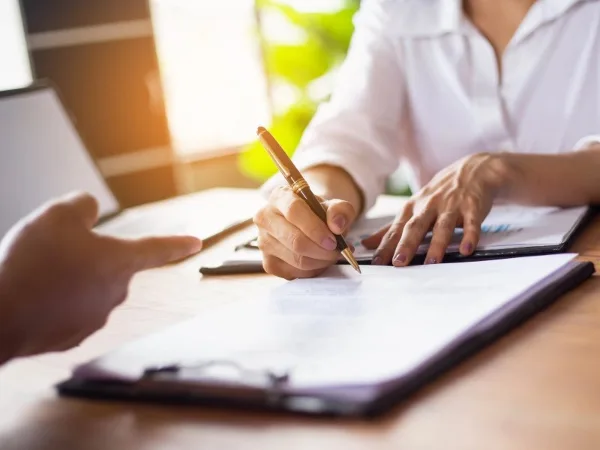 A person signing a legal document on a clipboard with a pen.