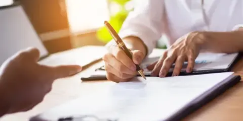 A person signing a legal document on a clipboard with a pen.