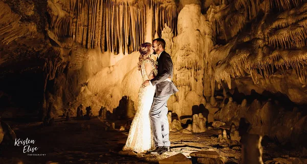 A bride and groom kissing inside a cave with illuminated rock formations.