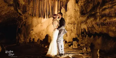 A bride and groom kissing inside a cave with illuminated rock formations.