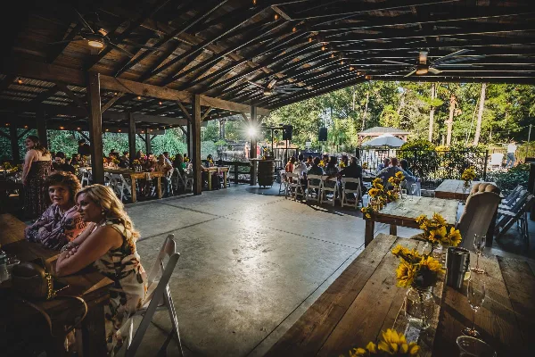 Interior view of a rustic wedding venue pavilion with wooden tables, string lights, and guests seated during an event.