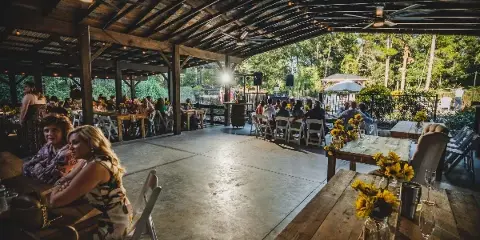 Interior view of a rustic wedding venue pavilion with wooden tables, string lights, and guests seated during an event.
